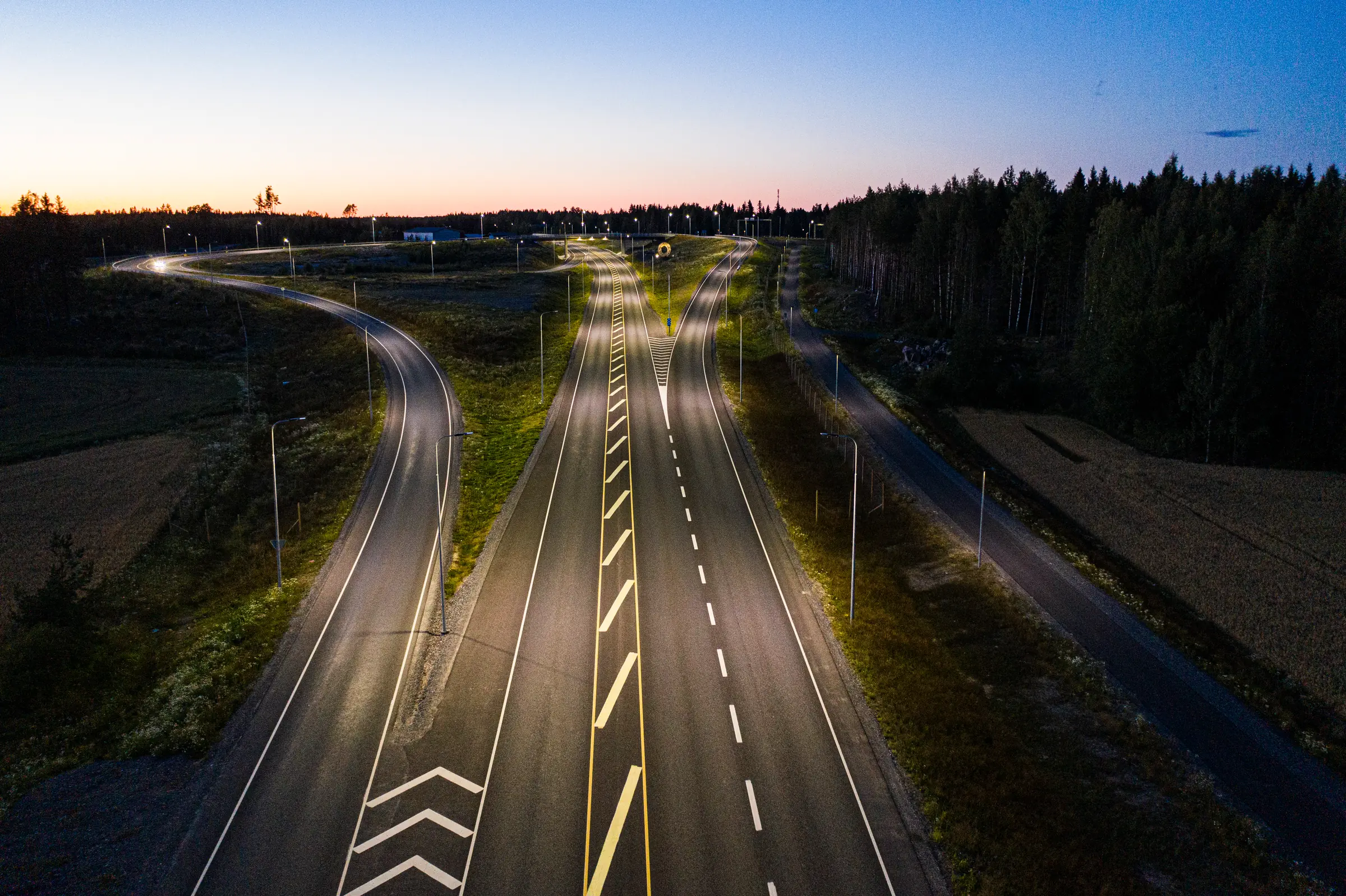 The Söörmarkku junction from above at dusk: the main road and its ramps run toward the interchange under rows of lit lighting poles.